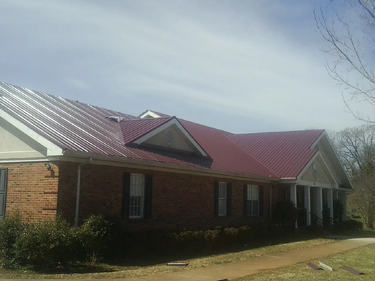 Red metal roof with gabled entries on a long brick building, from a Hail Damage Roof Repair job in Yorkville
