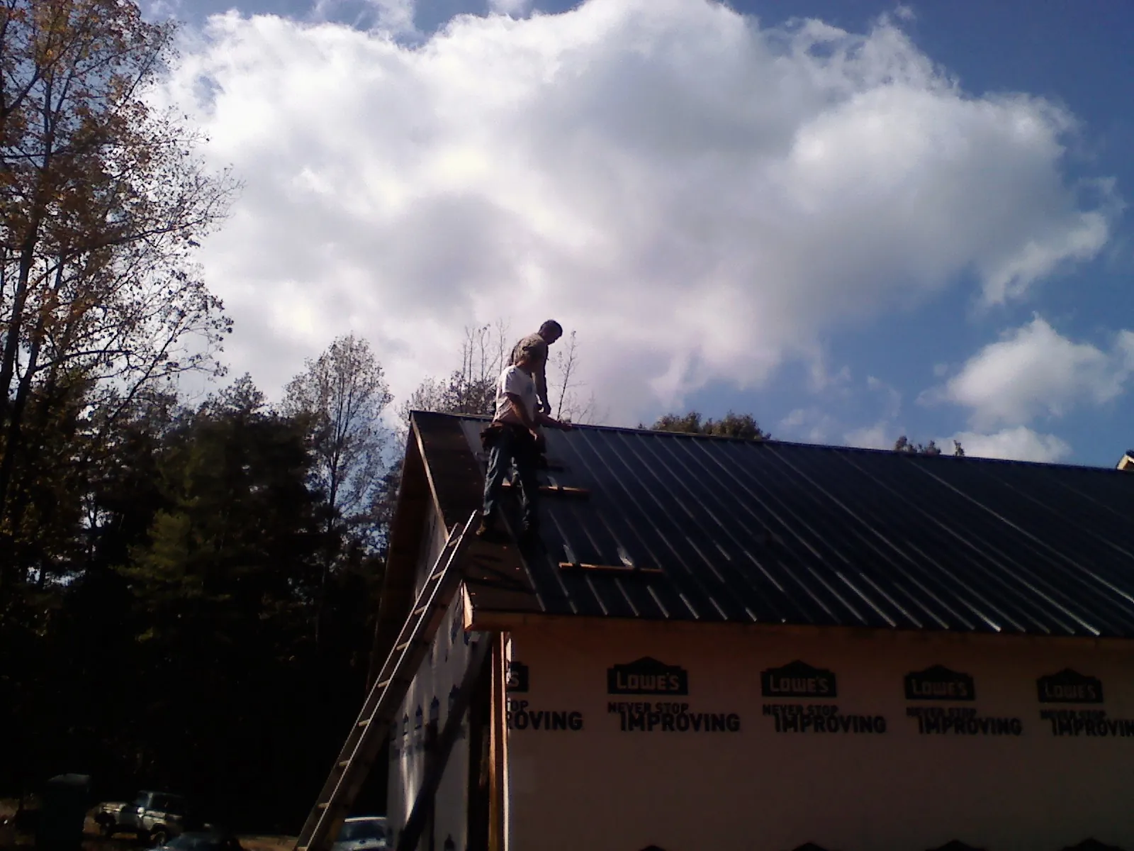Roofer fastening dark metal panels high against a cloudy sky, from a Roof Inspection job in Yorkville
