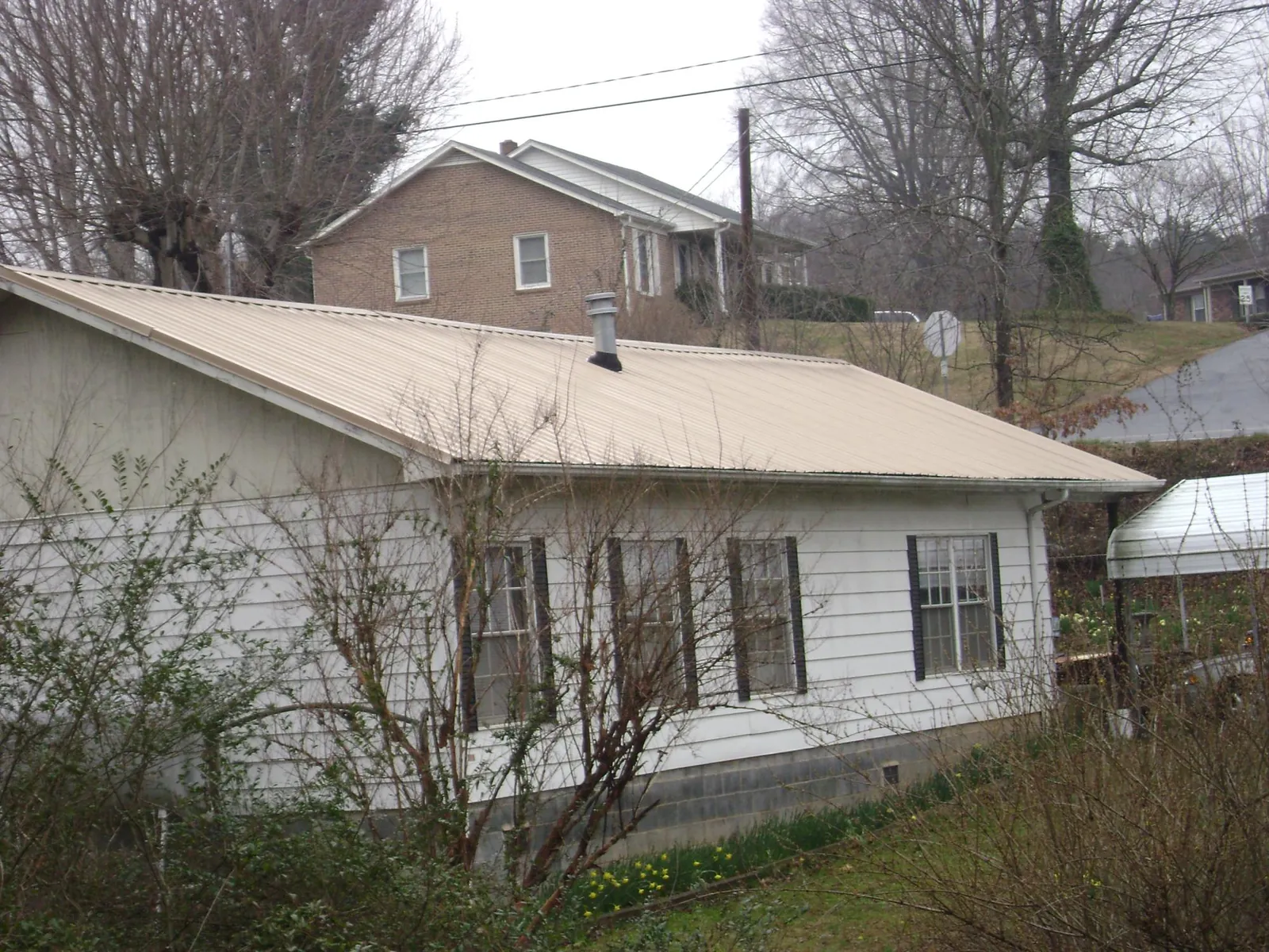 Tan metal roof on a white sided house set into a hillside — Commercial Roofing by Roofing Brothers in Yorkville